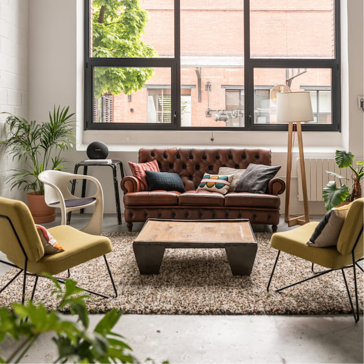 Pièce du studio photo comportant un canapé, une table basse et trois fauteuiles. Des plantes vertes sont réparties dans la pièce.